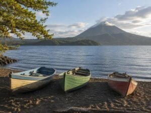 Three painted wooden fishing boats on a dark sand lakeshore with volcanic hills across the water in Nicaragua