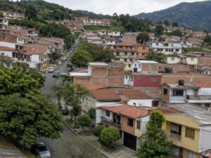 Aerial view of a present-day hillside residential neighborhood of brick and painted homes with red tile and flat roofs, trees and green mountains beyond in Colombia