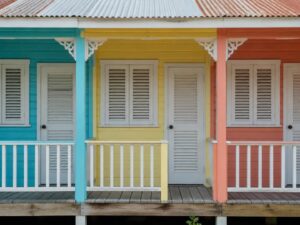 Three adjoining pastel wooden Caribbean-style house fronts with louvered shutters and a veranda in Belize