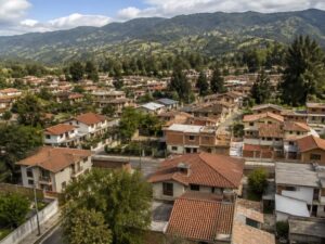Aerial view of a present-day residential neighborhood with red tile roofs, gardens and tall trees, with green mountains beyond in Ecuador
