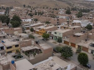 Aerial view of a residential neighborhood with brick and painted homes, flat roofs, trees and dry hills in Peru