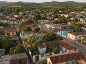Aerial view of a residential neighborhood with pastel homes, red tile and flat concrete roofs and palm trees below green hills in Cuba