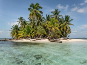 Tiny palm-covered sandy island with a wooden canoe on the shore in clear turquoise Caribbean water in Panama