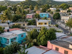 Aerial view of a residential neighborhood with turquoise, pink and yellow homes, flat roofs, palms and green hills in the Dominican Republic