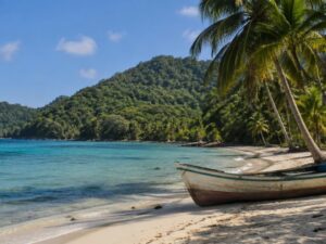 Quiet Caribbean bay with turquoise water, a wooden fishing boat on the sand, coconut palms and forested hills in Honduras