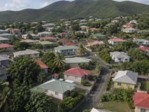 Aerial view of a residential neighborhood with single-story homes, colorful metal hip roofs, palms, and green hills in Saint Kitts and Nevis