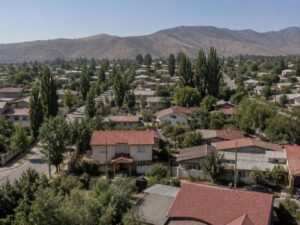 Aerial view of a present-day residential neighborhood with red tile roofs, gardens and tall poplar trees, with brown foothills beyond in Chile