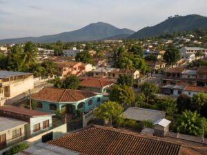 Aerial view of a residential neighborhood with tiled and metal roofs, trees, palms and volcanic hills in El Salvador