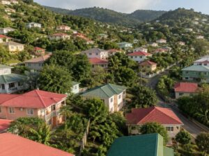 Aerial view of a hillside neighborhood with pastel homes, red and green metal roofs and a winding road in Grenada