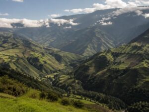 Green Andean highland valleys with small farm fields on steep slopes and clouds over the ridges in Ecuador
