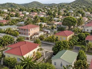 Aerial view of a residential neighborhood with pastel homes and red and green metal roofs among palm trees in Antigua and Barbuda