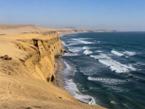 Golden desert sand cliffs meeting the blue Pacific Ocean and white surf on the coast of Peru