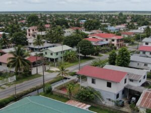 Aerial view of a residential neighborhood with wooden and concrete homes, metal roofs, palms and a drainage canal in Guyana