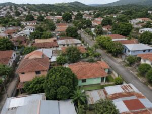Aerial view of a present-day residential neighborhood with pastel homes, tile and metal roofs, mango trees and green hills in Honduras
